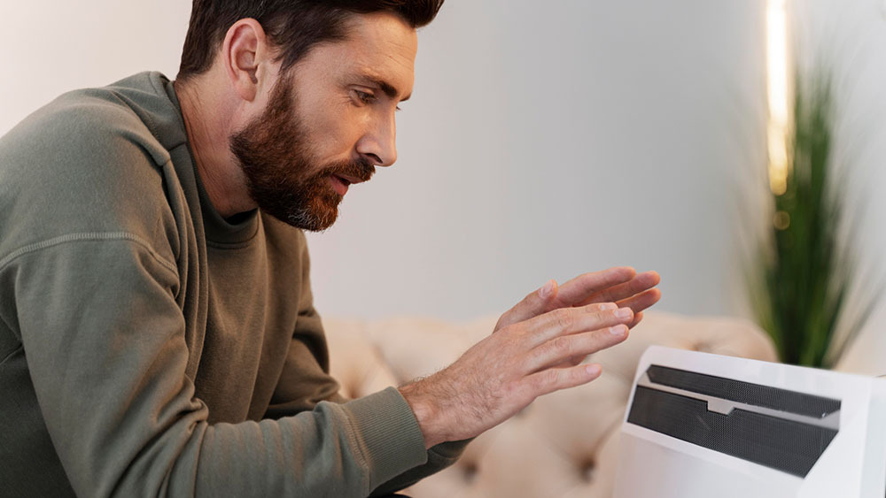 A man warming up his hands in front of a heater