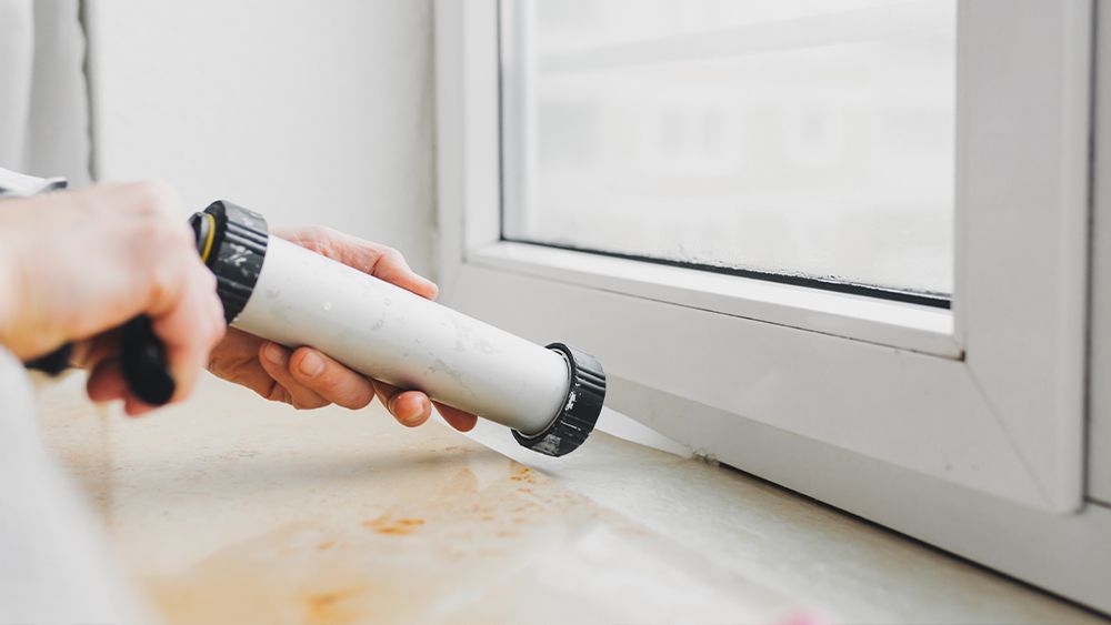 A man caulking a window to prevent heat loss