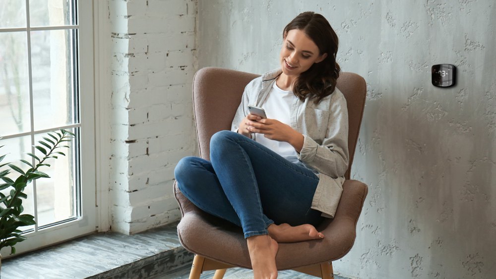 Woman using her phone - Cielo Breez Plus on the wall, maintaing ideal temperature. Control Best Through-The-Wall Air Conditioners using cielo breez.