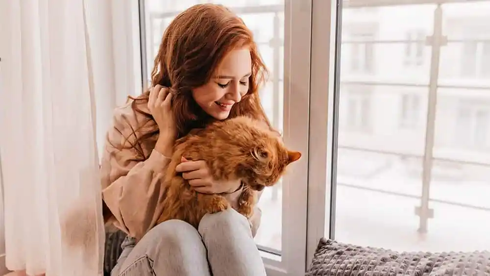 Woman with her cat sitting beside the window.