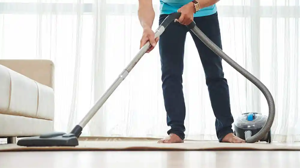 Man cleaning the room with a vacuum.