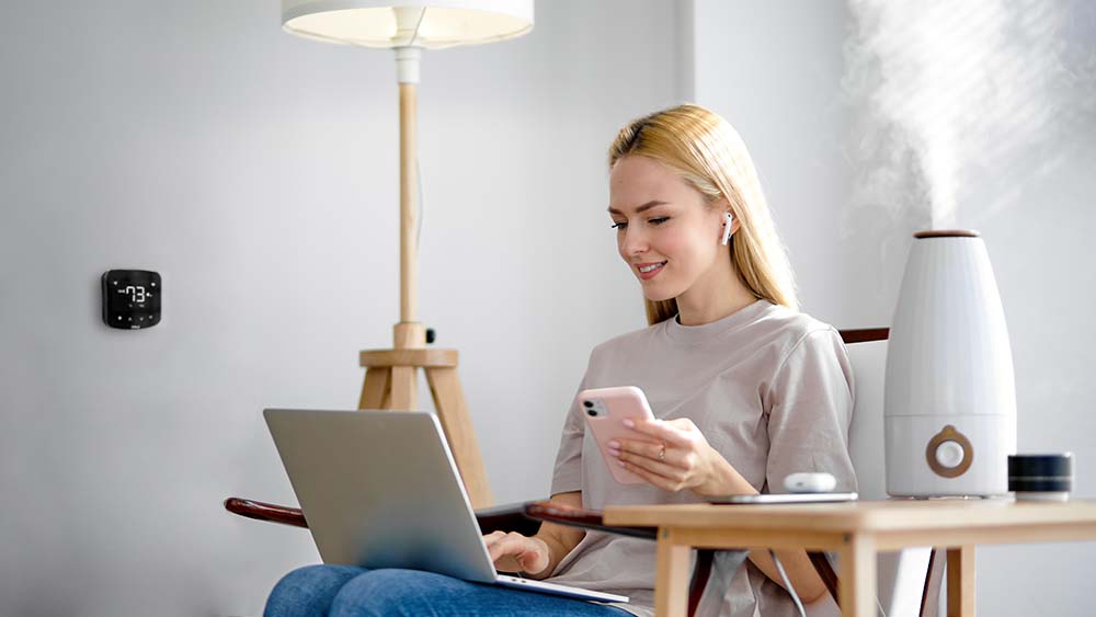 Woman working on her comouter. A humidifier is palced on a table, paired with Cielo Breez smart AC controller for maintaining ideal humidity levels